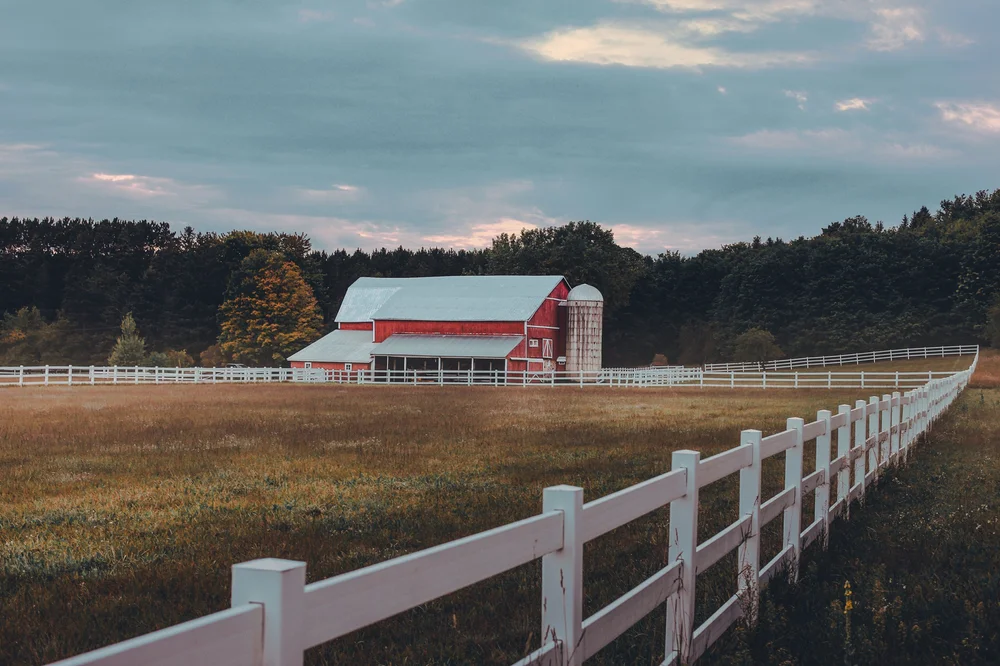 Red barn and white fence under an overcast sky